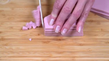 Kadın eli, tahta kesme tahtasının üzerinde beyaz bir seramik bıçakla sosis kesiyor.