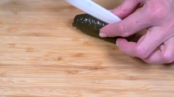 Kadın eli, tahta kesme tahtasına beyaz seramik bir bıçakla tuzlu salatalığı kesiyor. — Stok video