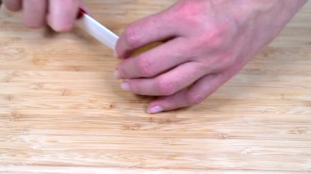 Samice ručně krájí brambory s bílým keramickým nožem na dřevěné řezací desce — Stock video