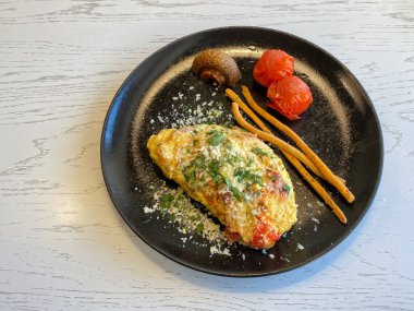 Siyah tabakta domuz pastırmalı, domatesli, mantarlı ve peynirli omlet.