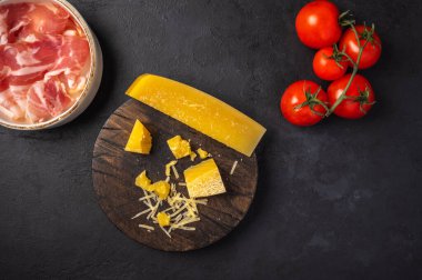 Kesme tahtasında dilimler ve rendelenmiş peynirli parmesan, beyaz seramik kasede jambon.