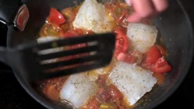 Kadın eli domates serer ve geleneksel Sicilya balığıyla vişneli spatulayı karıştırır.