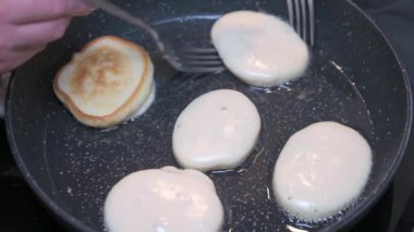 Kadın, kızgın yağlı tavada çatallı krep yapıyor.