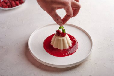 Kadınların elleri panna cotta 'ya nane yaprağı ve böğürtlen koyar.