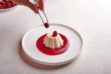 Kadın eli cımbızla panna cotta 'ya şerbetli ahududu koyar.