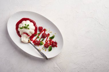 Bir parça panna cotta ile kaşık şuruplu, ahududu ve nane şekeri oval tabakta, yemek stili