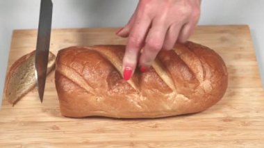 Kadın mutfak tahtasında bıçakla ekmek kesiyor.