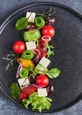 Domates, salatalık, bel biberi, zeytin ve siyah tabakta beyaz peynir ile taze Yunan salatası.