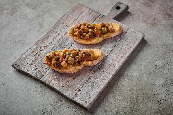 Bruschetta with homemade traditional Sicilian caponata and ciabatta bread on wooden cutting board