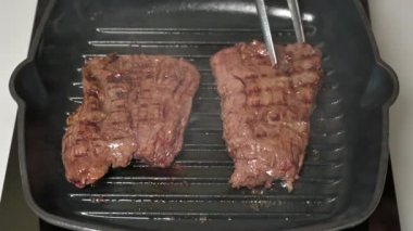 Female chef flips fried outside skirt beef steaks on hot grill pan with the ferry