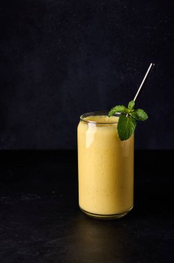 Dikey yönelim mango lassi cam içinde koyu arkaplanda tüp ile