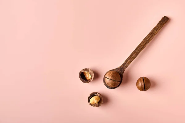 Macadamia ořech v dřevěné lžíce na růžovém práškovém pozadí — Stock fotografie