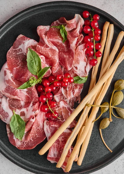 Food background prosciutto coppa di parma ham with basil, grissini sticks, capers and redcurrant — Stock Photo, Image