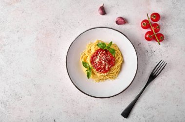 Domates soslu makarna, parmesan peyniri ve siyah çatalla beyaz tabakta fesleğen. 