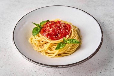 Domates soslu spagetti, beyaz tabakta parmesan peyniri ve fesleğen.