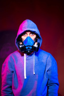 Bilinmeyen bir adamın portresi, karanlık arka planda neon maske takan bir hacker. Neon ışıklandırması yakınında silah tutan çift ırklı siber punk oyuncusunun seçici odak noktası