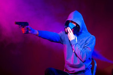 Bilinmeyen bir adamın portresi, karanlık arka planda neon maske takan bir hacker. Neon ışıklandırması yakınında silah tutan çift ırklı siber punk oyuncusunun seçici odak noktası