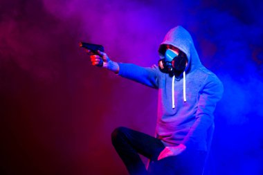 Bilinmeyen bir adamın portresi, karanlık arka planda neon maske takan bir hacker. Neon ışıklandırması yakınında silah tutan çift ırklı siber punk oyuncusunun seçici odak noktası