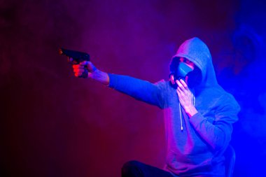 Bilinmeyen bir adamın portresi, karanlık arka planda neon maske takan bir hacker. Neon ışıklandırması yakınında silah tutan çift ırklı siber punk oyuncusunun seçici odak noktası