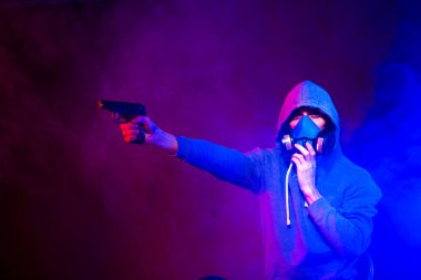 Bilinmeyen bir adamın portresi, karanlık arka planda neon maske takan bir hacker. Neon ışıklandırması yakınında silah tutan çift ırklı siber punk oyuncusunun seçici odak noktası