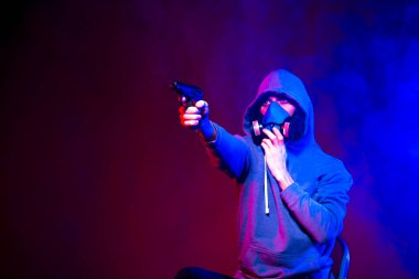 Bilinmeyen bir adamın portresi, karanlık arka planda neon maske takan bir hacker. Neon ışıklandırması yakınında silah tutan çift ırklı siber punk oyuncusunun seçici odak noktası