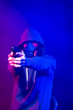 Bilinmeyen bir adamın portresi, karanlık arka planda neon maske takan bir hacker. Neon ışıklandırması yakınında silah tutan çift ırklı siber punk oyuncusunun seçici odak noktası