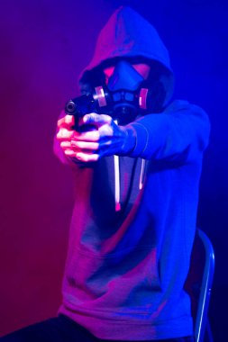 Bilinmeyen bir adamın portresi, karanlık arka planda neon maske takan bir hacker. Neon ışıklandırması yakınında silah tutan çift ırklı siber punk oyuncusunun seçici odak noktası