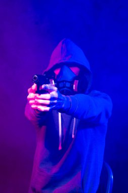 Bilinmeyen bir adamın portresi, karanlık arka planda neon maske takan bir hacker. Neon ışıklandırması yakınında silah tutan çift ırklı siber punk oyuncusunun seçici odak noktası