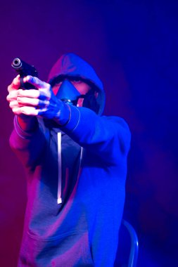 Bilinmeyen bir adamın portresi, karanlık arka planda neon maske takan bir hacker. Neon ışıklandırması yakınında silah tutan çift ırklı siber punk oyuncusunun seçici odak noktası