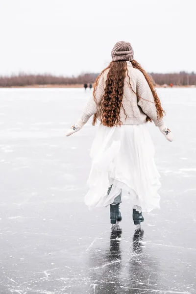 Woman ice skating outdoors on a pond. Outdoors lifestyle portrait of girl in figured skates. Smiling and enjoying wintertime. Wearing stylish down sweater, skirt, knitted mittens. Ready for skating