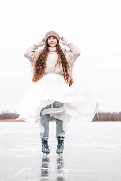 Woman ice skating outdoors on a pond. Outdoors lifestyle portrait of girl in figured skates. Smiling and enjoying wintertime. Wearing stylish down sweater, skirt, knitted mittens. Ready for skating