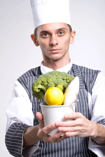 Aufgeregte Mann Koch Uniform Hält Einen Eimer Mit Gemüse Isoliert — Stockfoto