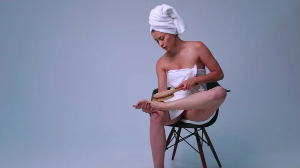 穿着白毛巾 穿着灰色背景衣服的性感女孩 视频中美丽的女性与苗条的身材 应用按摩刷在身体上 美容美发 温泉及身体护理的概念 — 图库照片