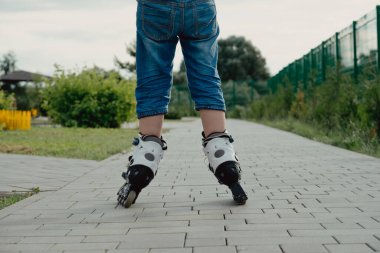 Koruyucu ekipman ve patenler içinde küçük bir çocuk parkta yürüyüş yolunda duruyor, alçak açılı.