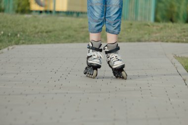 Koruyucu ekipman ve patenler içinde küçük bir çocuk parkta yürüyüş yolunda duruyor, alçak açılı.