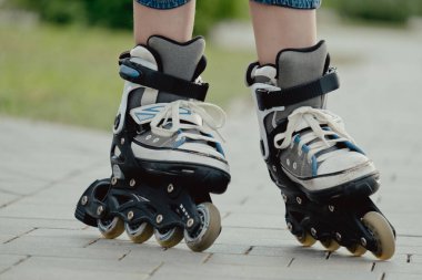 Koruyucu ekipman ve patenler içinde küçük bir çocuk parkta yürüyüş yolunda duruyor, alçak açılı.