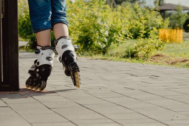 Koruyucu ekipman ve patenler içinde küçük bir çocuk parkta yürüyüş yolunda duruyor, alçak açılı.