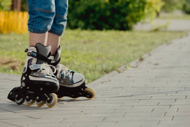 Koruyucu ekipman ve patenler içinde küçük bir çocuk parkta yürüyüş yolunda duruyor, alçak açılı.