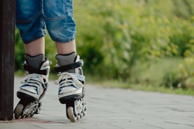 Koruyucu ekipman ve patenler içinde küçük bir çocuk parkta yürüyüş yolunda duruyor, alçak açılı.