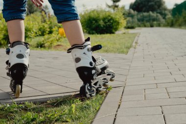 Koruyucu ekipman ve patenler içinde küçük bir çocuk parkta yürüyüş yolunda duruyor, alçak açılı.