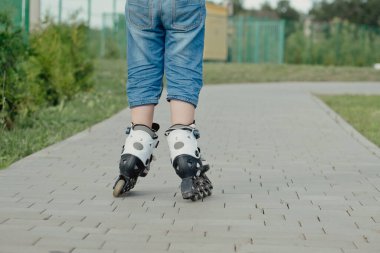 Koruyucu ekipman ve patenler içinde küçük bir çocuk parkta yürüyüş yolunda duruyor, alçak açılı.