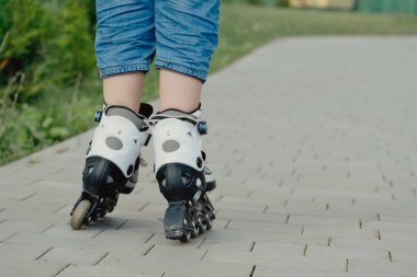 Koruyucu ekipman ve patenler içinde küçük bir çocuk parkta yürüyüş yolunda duruyor, alçak açılı.