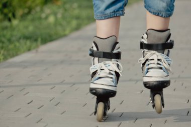 Koruyucu ekipman ve patenler içinde küçük bir çocuk parkta yürüyüş yolunda duruyor, alçak açılı.