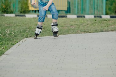 Koruyucu ekipman ve patenler içinde küçük bir çocuk parkta yürüyüş yolunda duruyor, alçak açılı.