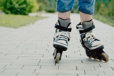 Koruyucu ekipman ve patenler içinde küçük bir çocuk parkta yürüyüş yolunda duruyor, alçak açılı.