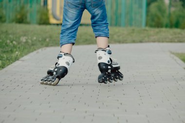 Koruyucu ekipman ve patenler içinde küçük bir çocuk parkta yürüyüş yolunda duruyor, alçak açılı.