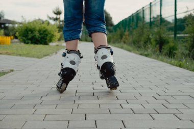 Koruyucu ekipman ve patenler içinde küçük bir çocuk parkta yürüyüş yolunda duruyor, alçak açılı.