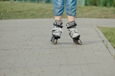 Koruyucu ekipman ve patenler içinde küçük bir çocuk parkta yürüyüş yolunda duruyor, alçak açılı.