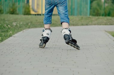 Koruyucu ekipman ve patenler içinde küçük bir çocuk parkta yürüyüş yolunda duruyor, alçak açılı.