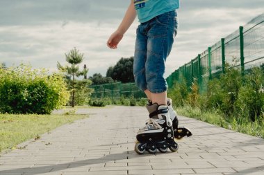 Koruyucu ekipman ve patenler içinde küçük bir çocuk parkta yürüyüş yolunda duruyor, alçak açılı.